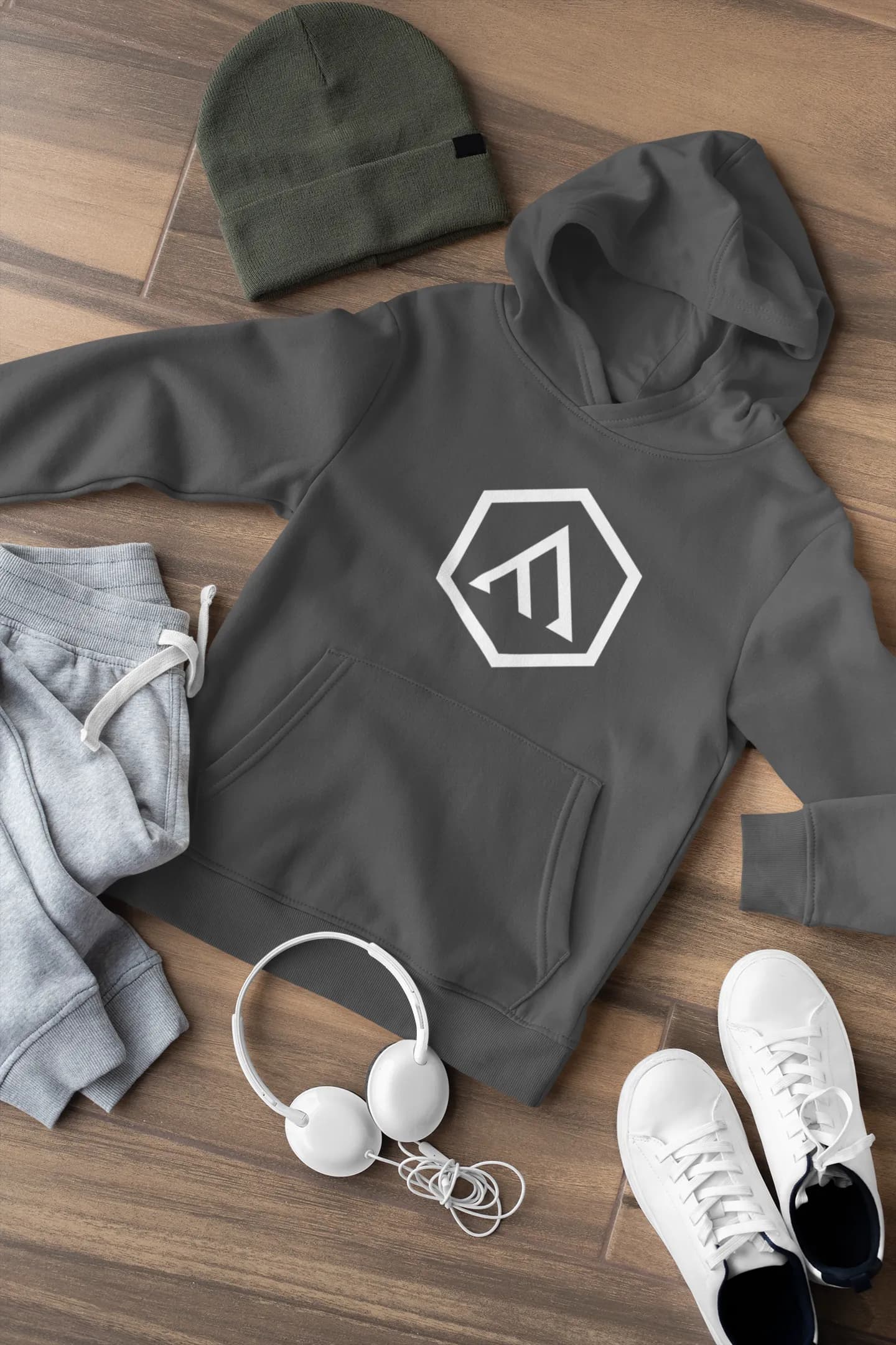 Branded hoodie flat-lay with beanie, headphones, and sneakers on a wood surface